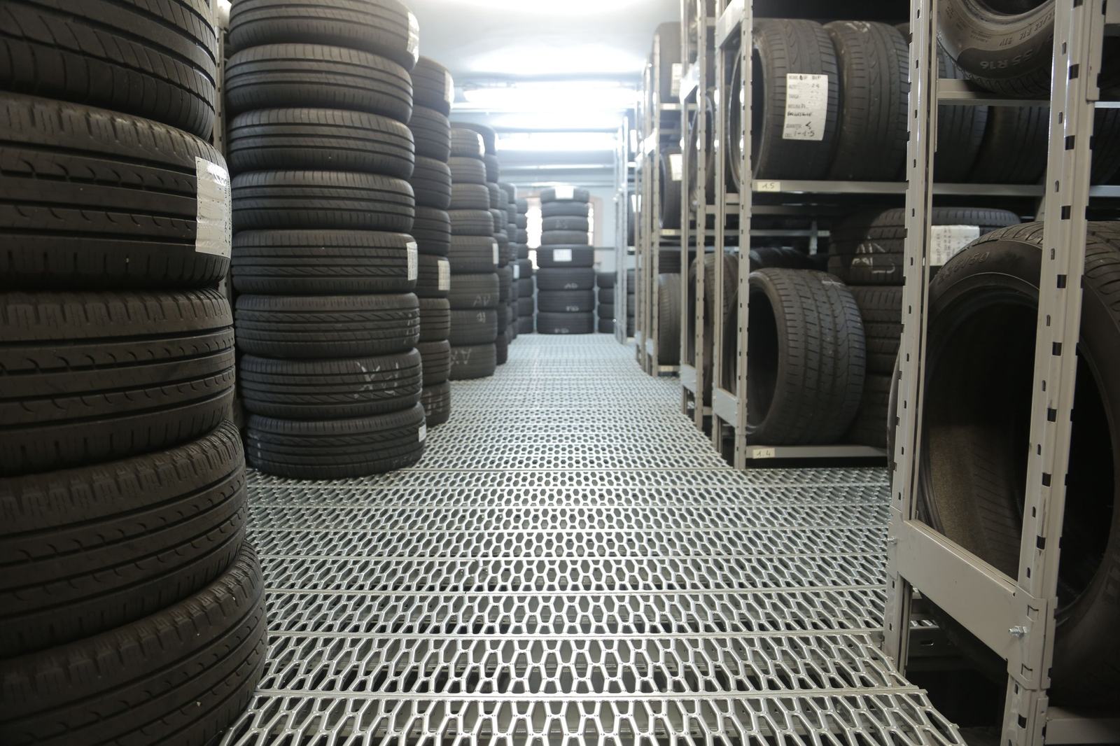 Corsia interna di un magazzino di pneumatici: pile di gomme e scaffalature metalliche cariche su entrambi i lati.